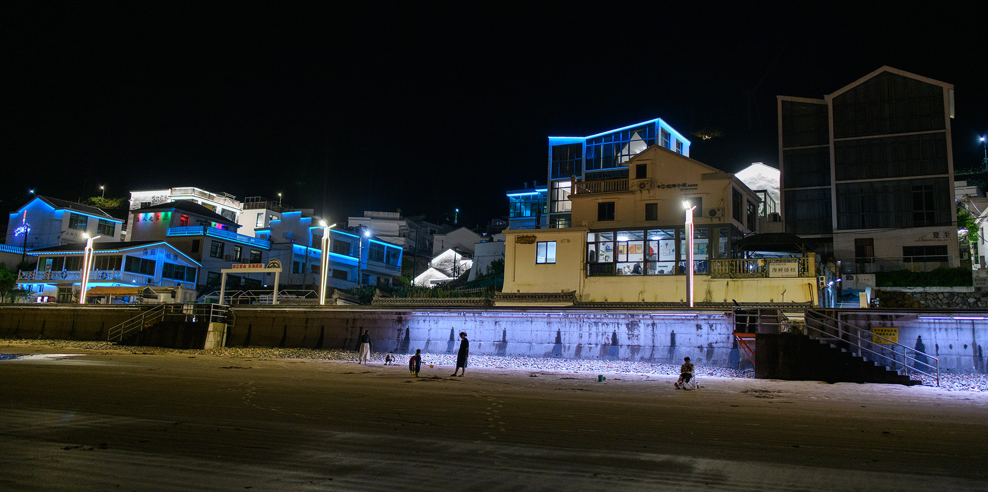 夜晚的海边民宿与餐厅，蓝色霓虹灯闪烁