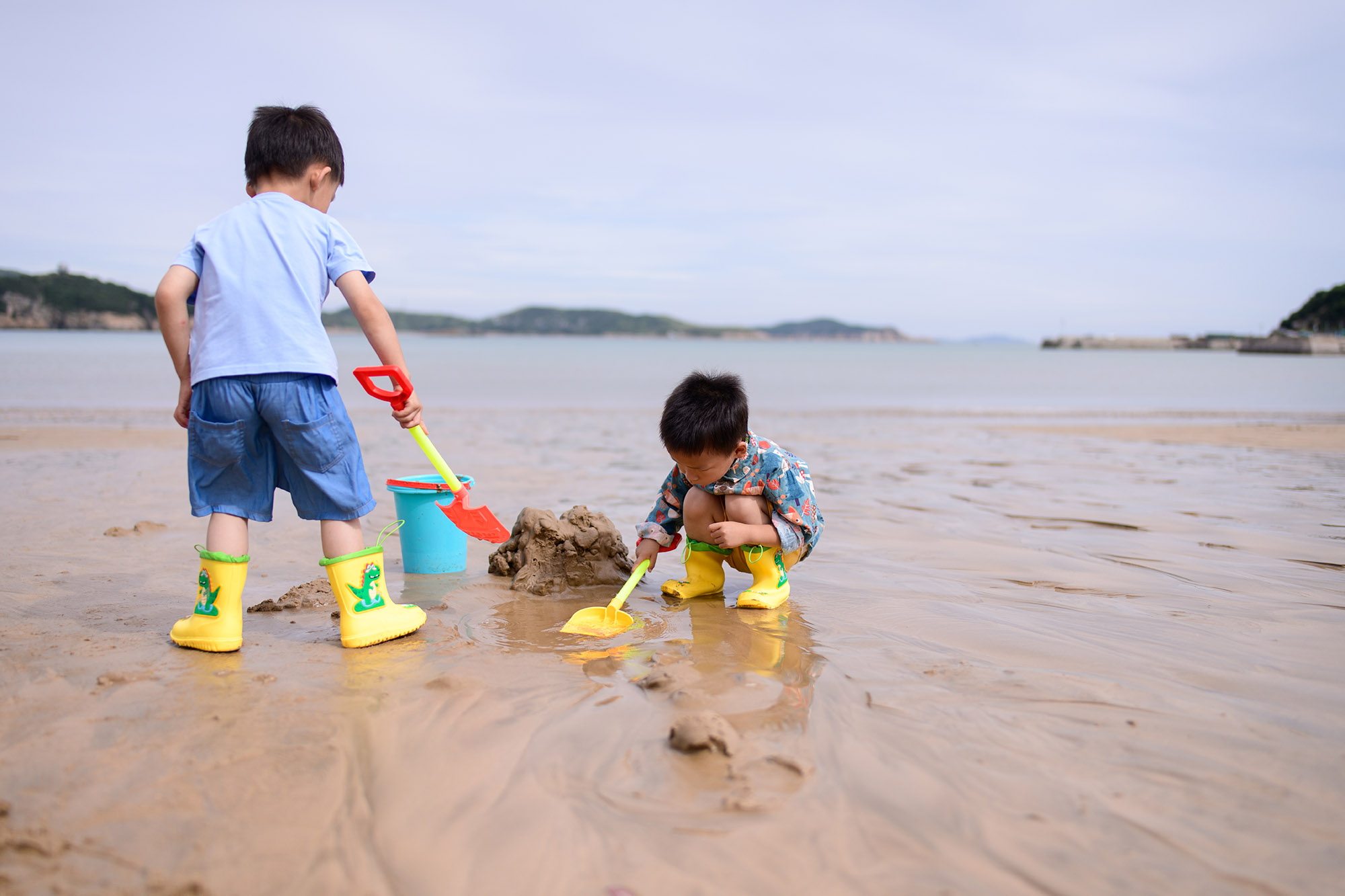 两个穿着雨靴的小男孩在沙龙沙滩上玩沙