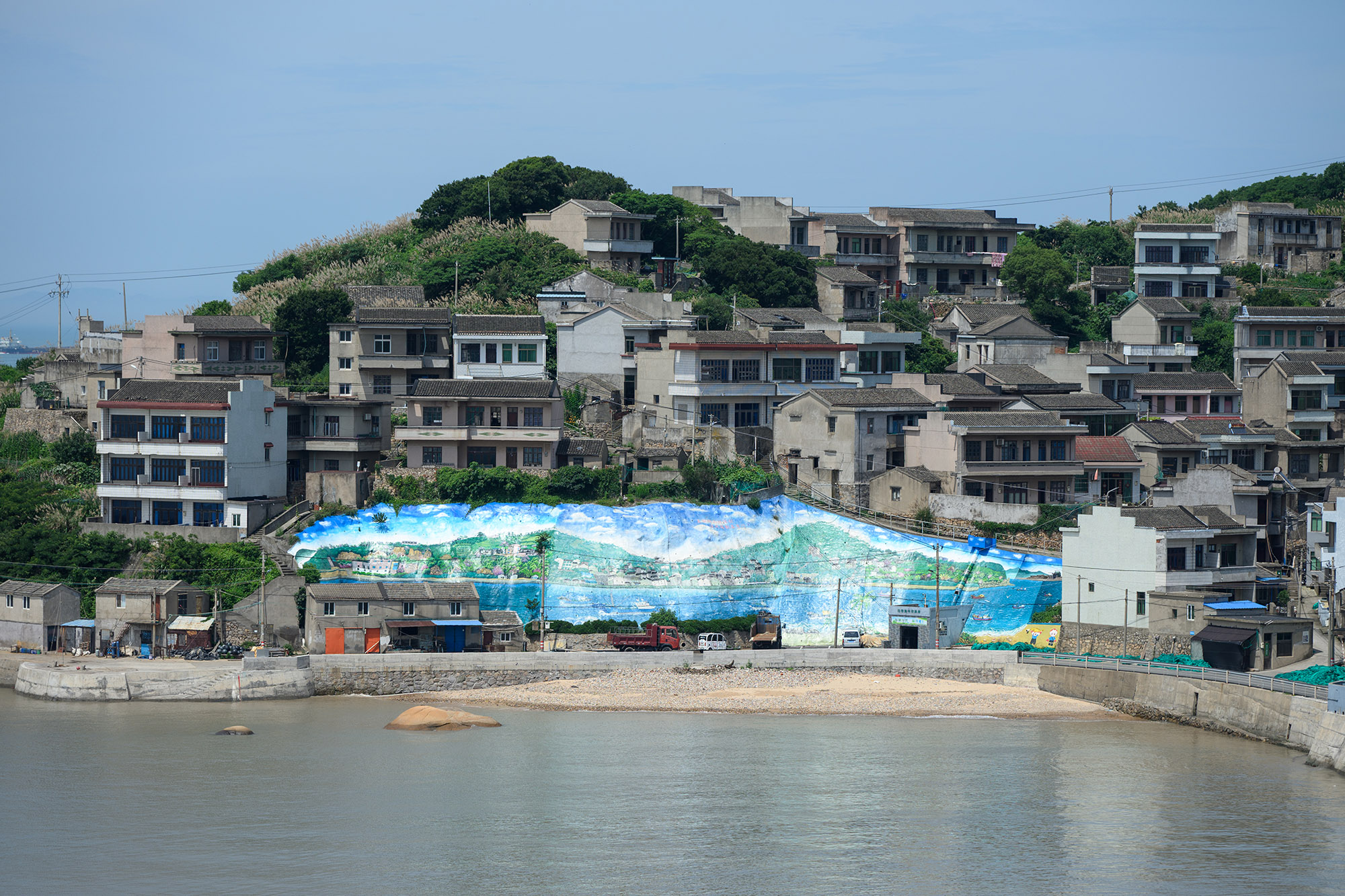依山而建的渔村，墙面上绘有巨大的蓝色海洋壁画